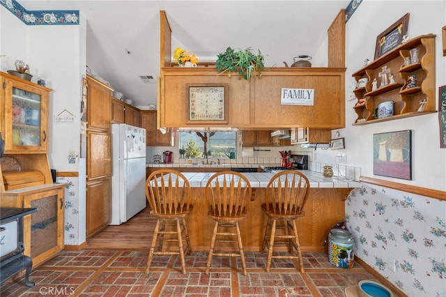 kitchen with sink, a breakfast bar area, white fridge, tile counters, and kitchen peninsula