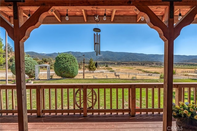 wooden terrace with a rural view, a mountain view, and a yard