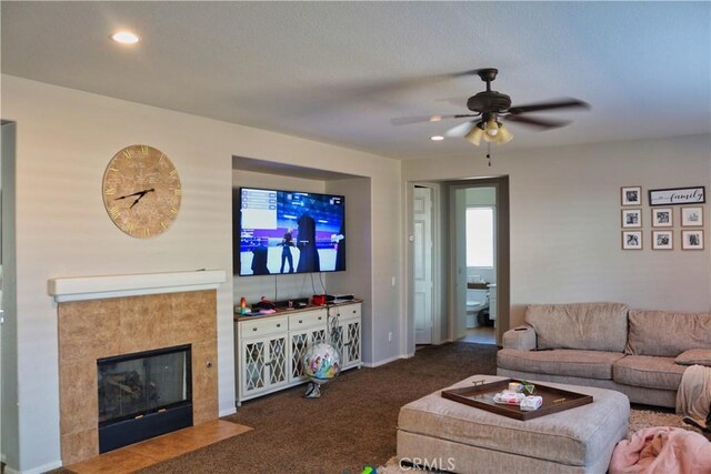 carpeted living room with a textured ceiling, a tiled fireplace, and ceiling fan