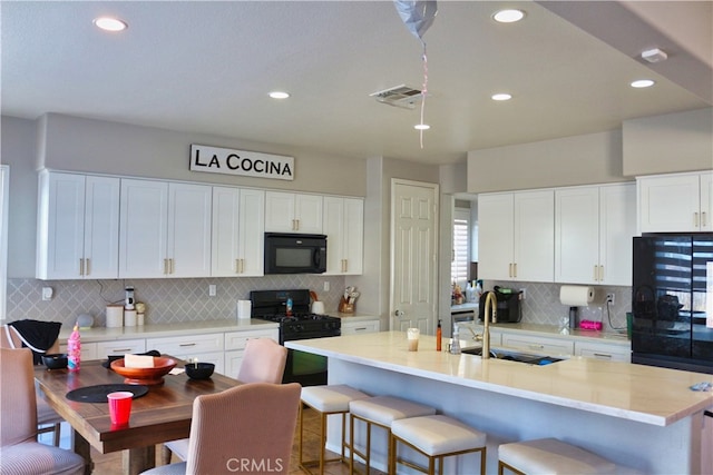 kitchen with white cabinets, a center island with sink, sink, and black appliances