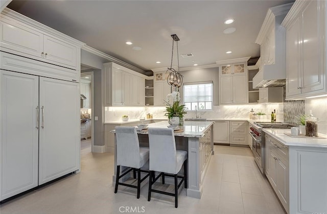 kitchen with backsplash, premium range hood, premium appliances, a kitchen island, and white cabinetry