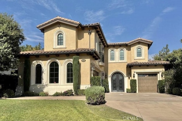 mediterranean / spanish house featuring a garage, a tile roof, concrete driveway, french doors, and a front lawn