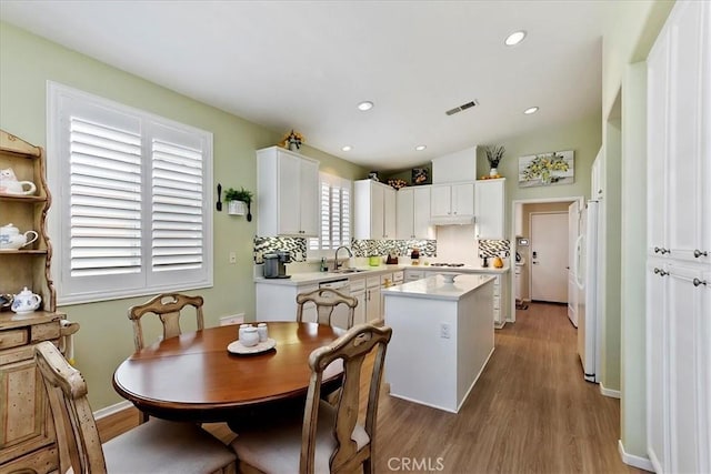 kitchen featuring a sink, visible vents, light countertops, backsplash, and a center island