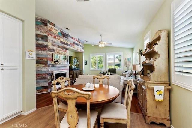 dining space with a fireplace, lofted ceiling, visible vents, light wood-style flooring, and ceiling fan