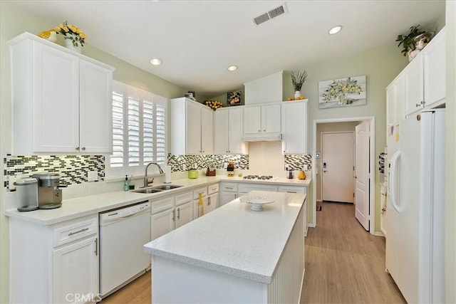 kitchen with white appliances, a kitchen island, a sink, visible vents, and white cabinetry