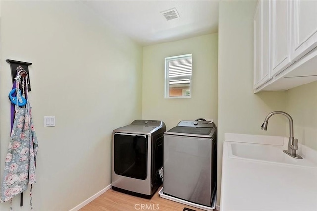 washroom featuring cabinet space, light wood finished floors, visible vents, independent washer and dryer, and a sink