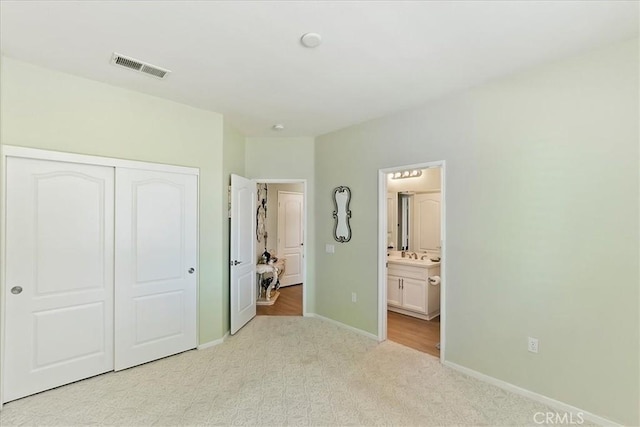 unfurnished bedroom featuring ensuite bathroom, light colored carpet, visible vents, baseboards, and a closet