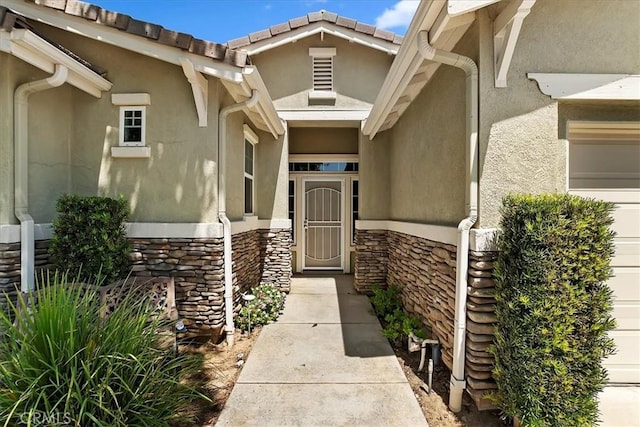 property entrance with a garage, stone siding, a tile roof, and stucco siding