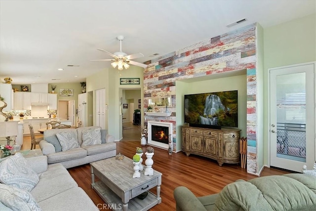 living area featuring a fireplace, wood finished floors, visible vents, and a ceiling fan