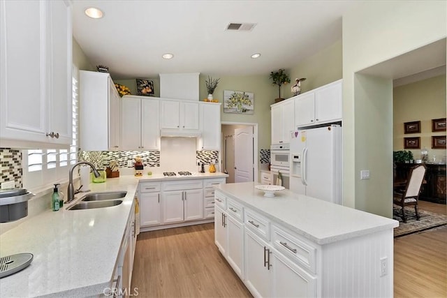 kitchen featuring a center island, visible vents, light wood-style flooring, a sink, and white appliances