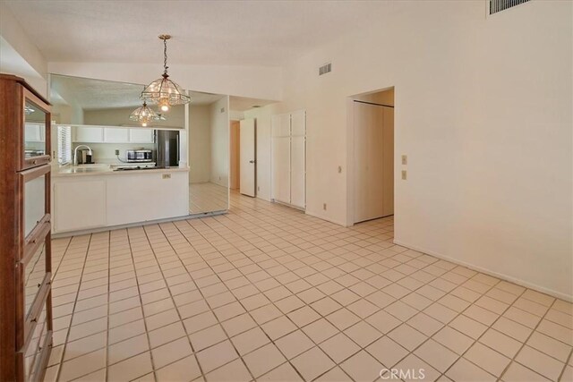 interior space featuring stainless steel appliances, hanging light fixtures, vaulted ceiling, white cabinets, and sink