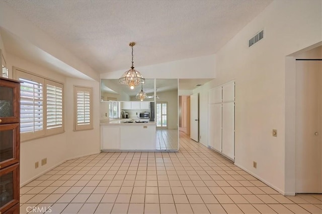 kitchen with white cabinets, lofted ceiling, hanging light fixtures, a chandelier, and light tile patterned floors