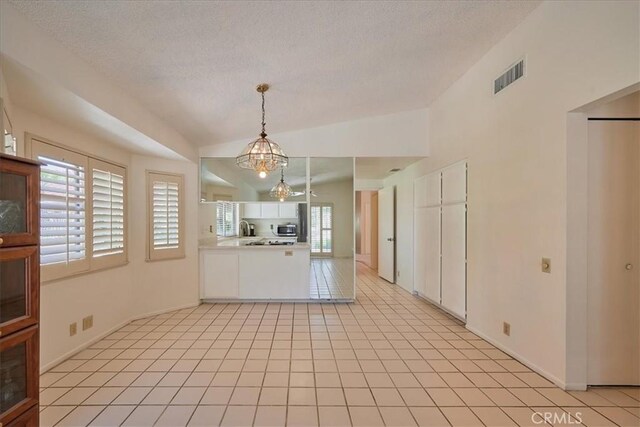 kitchen featuring an inviting chandelier, vaulted ceiling, hanging light fixtures, light tile patterned floors, and white cabinets