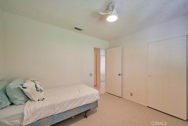 bedroom featuring ceiling fan, light carpet, and a textured ceiling