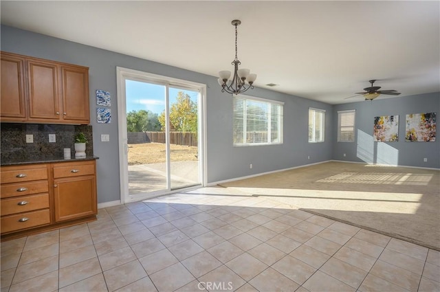 unfurnished dining area featuring ceiling fan with notable chandelier and light colored carpet