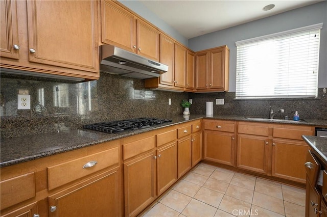 kitchen with gas cooktop, backsplash, sink, light tile patterned floors, and dark stone countertops