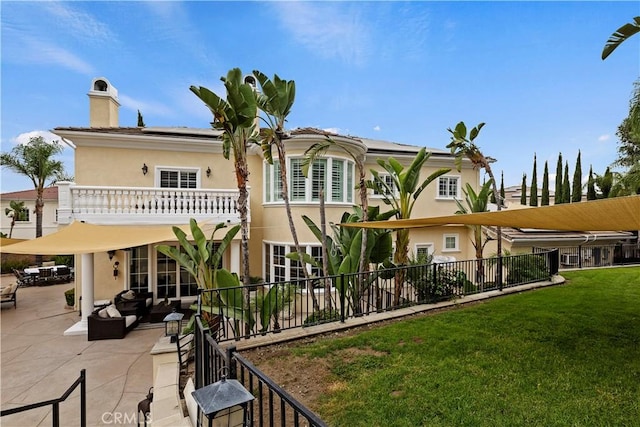 back of property with a balcony, outdoor lounge area, a patio, and a lawn