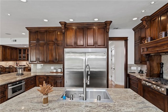 kitchen featuring dark brown cabinetry, sink, light stone counters, stainless steel appliances, and decorative backsplash