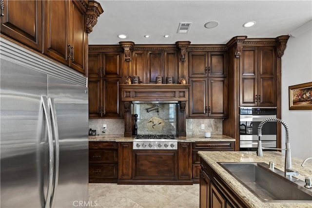 kitchen featuring sink, light stone counters, tasteful backsplash, dark brown cabinets, and stainless steel appliances