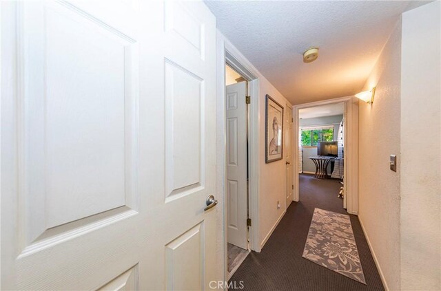 hallway featuring dark colored carpet and a textured ceiling