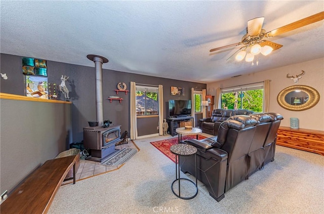 living room with a wood stove, ceiling fan, light colored carpet, and a textured ceiling