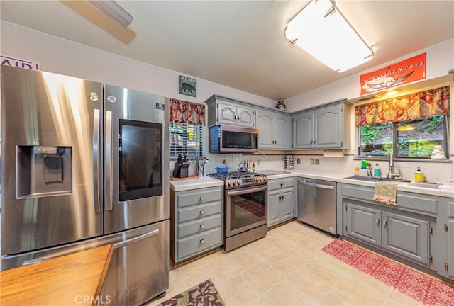 kitchen with gray cabinetry, sink, stainless steel appliances, and tasteful backsplash