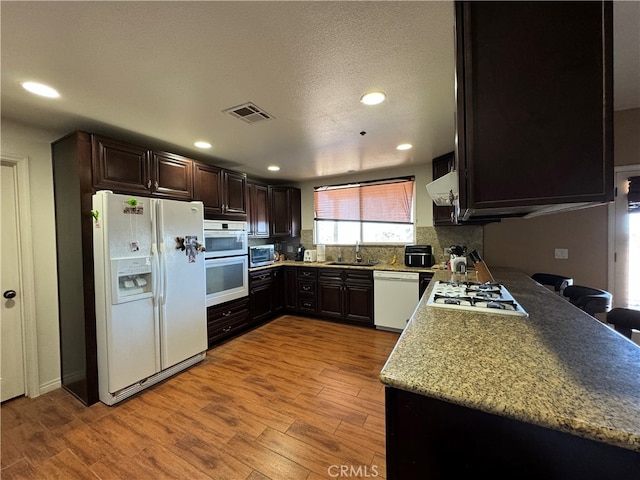 kitchen featuring backsplash, white appliances, light stone countertops, light wood-type flooring, and sink