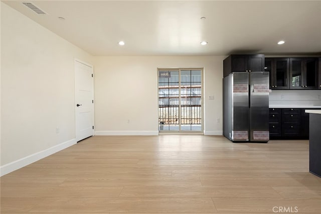 kitchen featuring light wood-type flooring, visible vents, dark cabinets, and freestanding refrigerator