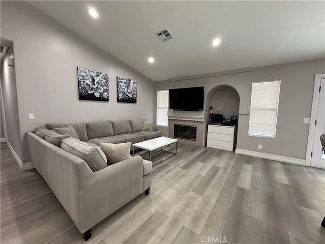 living room featuring lofted ceiling, plenty of natural light, a tile fireplace, and light hardwood / wood-style flooring