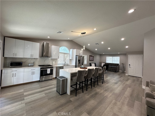 kitchen featuring appliances with stainless steel finishes, wall chimney exhaust hood, white cabinetry, and a healthy amount of sunlight