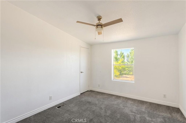 unfurnished room featuring baseboards, visible vents, dark carpet, and a ceiling fan