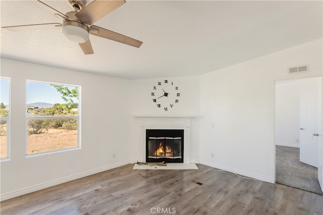 unfurnished living room featuring wood finished floors, a glass covered fireplace, and visible vents