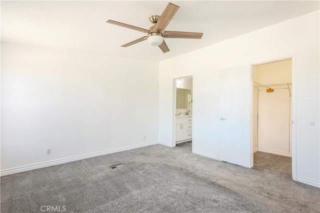 unfurnished bedroom featuring carpet floors, a spacious closet, baseboards, and ensuite bathroom