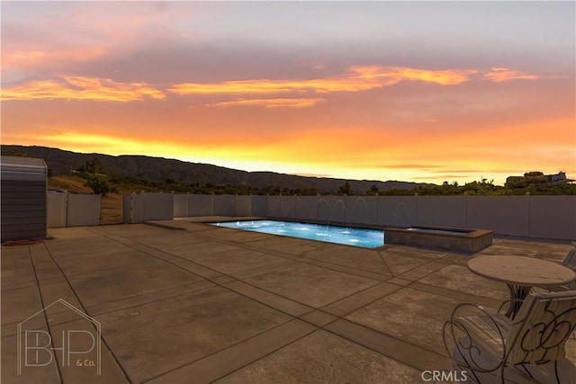 pool at dusk with a mountain view, an in ground hot tub, fence, a fenced in pool, and a patio area