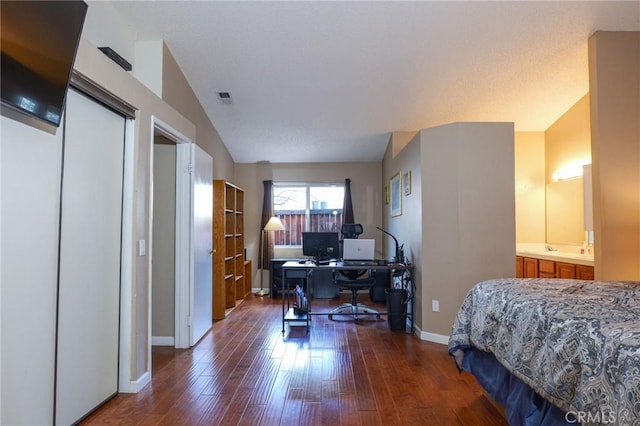 bedroom with dark hardwood / wood-style flooring, vaulted ceiling, and connected bathroom