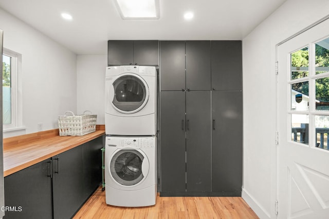 washroom featuring cabinets, light wood-type flooring, plenty of natural light, and stacked washer and dryer