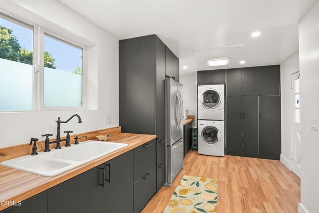 washroom with sink, light wood-type flooring, and stacked washer / drying machine