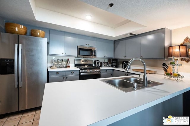 kitchen with sink, a textured ceiling, a tray ceiling, kitchen peninsula, and stainless steel appliances