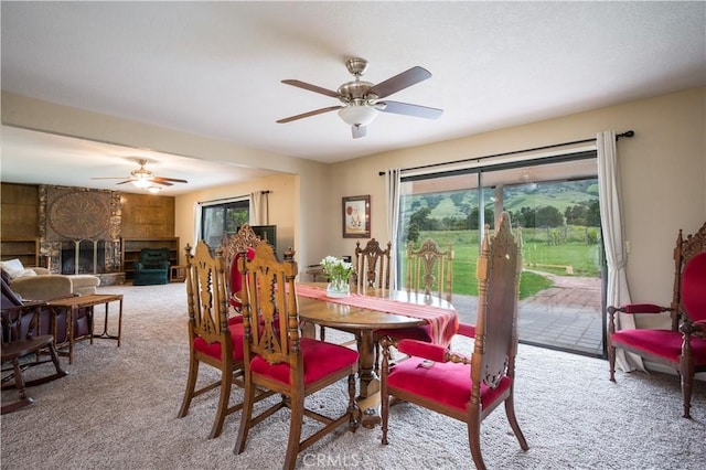 dining space featuring a stone fireplace, a healthy amount of sunlight, light carpet, and ceiling fan