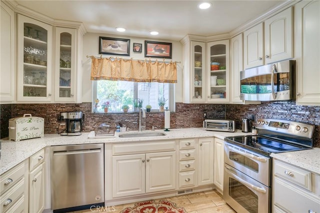 kitchen featuring sink, appliances with stainless steel finishes, tasteful backsplash, light stone countertops, and light hardwood / wood-style floors