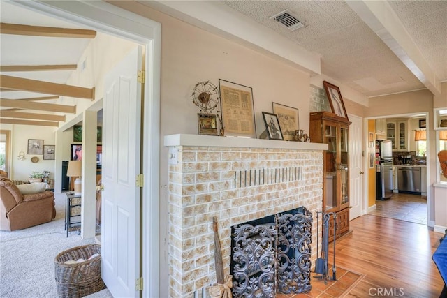 living room featuring a brick fireplace, beam ceiling, wood-type flooring, and a textured ceiling