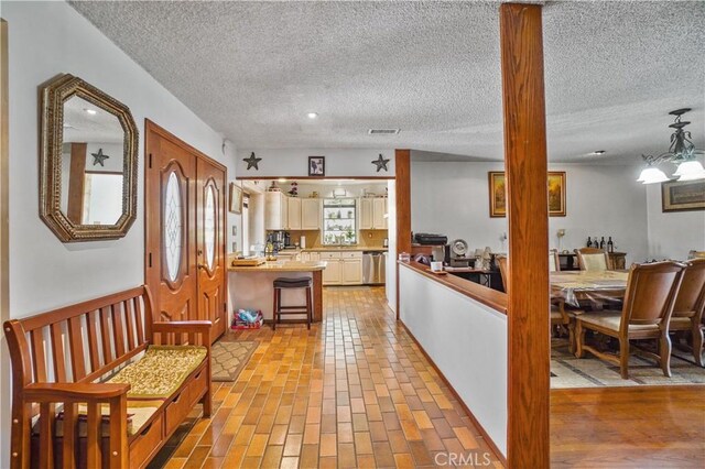 kitchen featuring an inviting chandelier, hanging light fixtures, stainless steel dishwasher, a textured ceiling, and kitchen peninsula