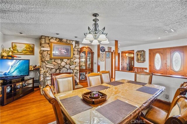 dining space with light wood-type flooring, a textured ceiling, an inviting chandelier, and a fireplace