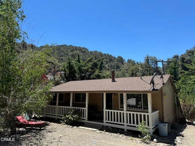 view of front facade with a wooded view, a porch, and roof with shingles