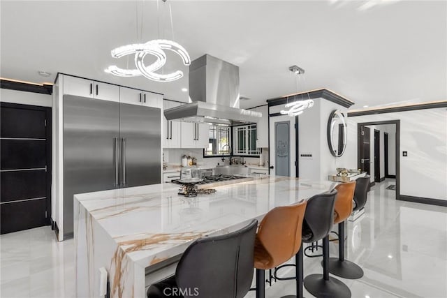 kitchen with island exhaust hood, light stone counters, white cabinets, and an inviting chandelier