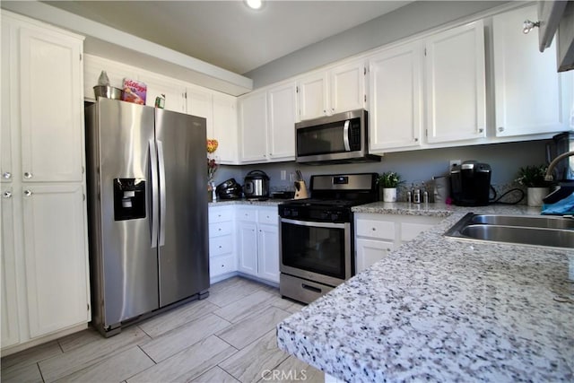 kitchen featuring light stone countertops, appliances with stainless steel finishes, white cabinetry, and sink