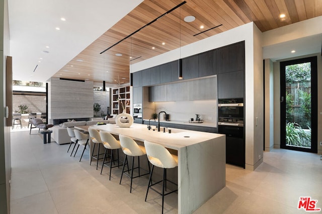 kitchen featuring tasteful backsplash, an island with sink, oven, hanging light fixtures, and wooden ceiling