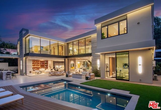 back house at dusk with a swimming pool with hot tub, outdoor lounge area, and a patio