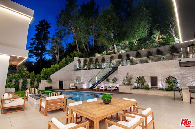 pool at night with a fire pit and a patio area