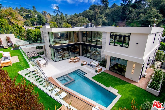 rear view of property with a yard, a patio area, an outdoor living space with a fire pit, and an in ground hot tub